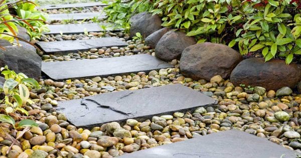 A garden path with big and flat rectangular stepping stones, set among two to 4 inch round river bed stones