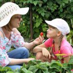 A mother and young girl picking a strawberry in a garden
