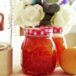 two glass jars of rosehip Jelly near vase of flowers