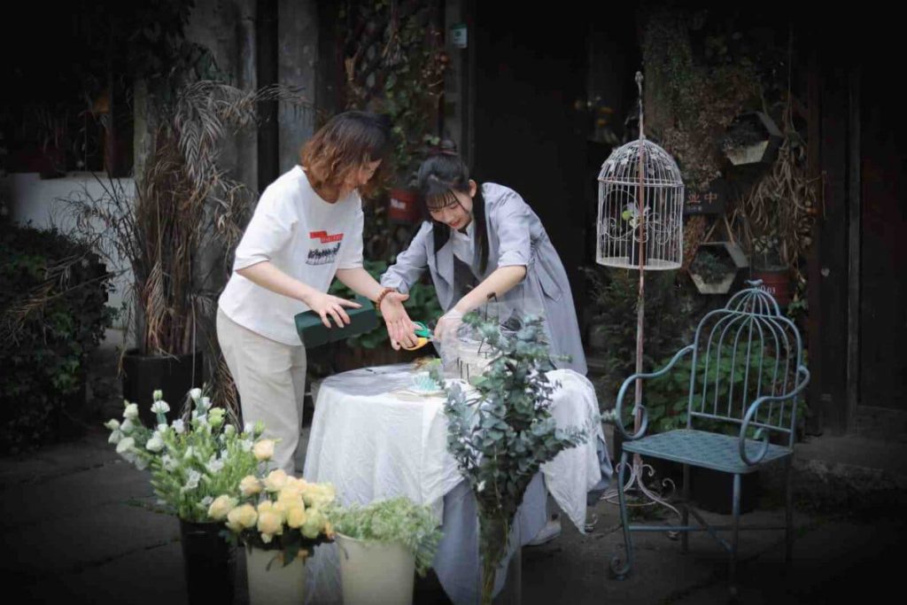 Two women, a senior with potentially a daughter, pruning a plant in a beautiful backyard setting