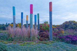 Multiple hydro poles, each in a different color, in a pollinator colorful garden