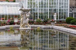 White greenhouse reflected in pond with statue