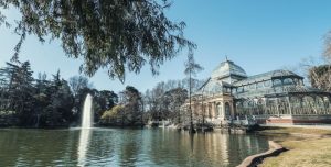 A large, classic greenhouse in front of a lsamll lake with a fountain