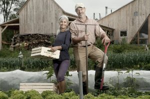 Man and woman farmers in a field with a farm in the background