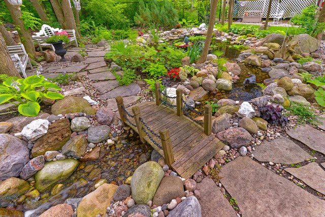 A stream with a walking bridge flowing into a backyard pond