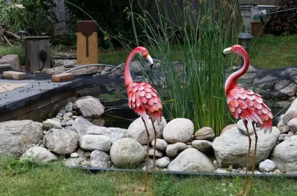 Two flamingo art pieces beside a pond